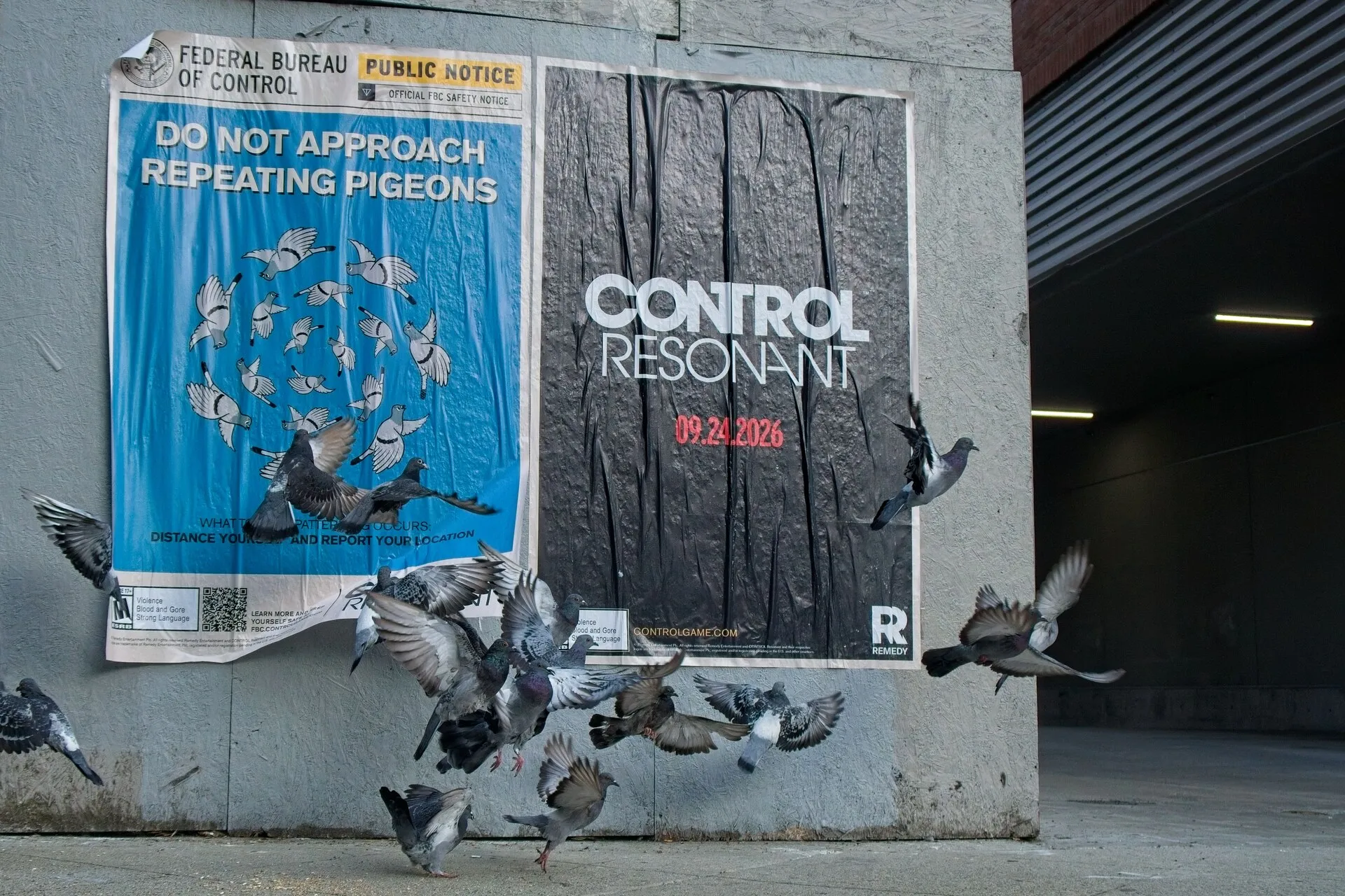 Pigeons fly in front of large posters on a concrete wall beside a dark garage entrance.
